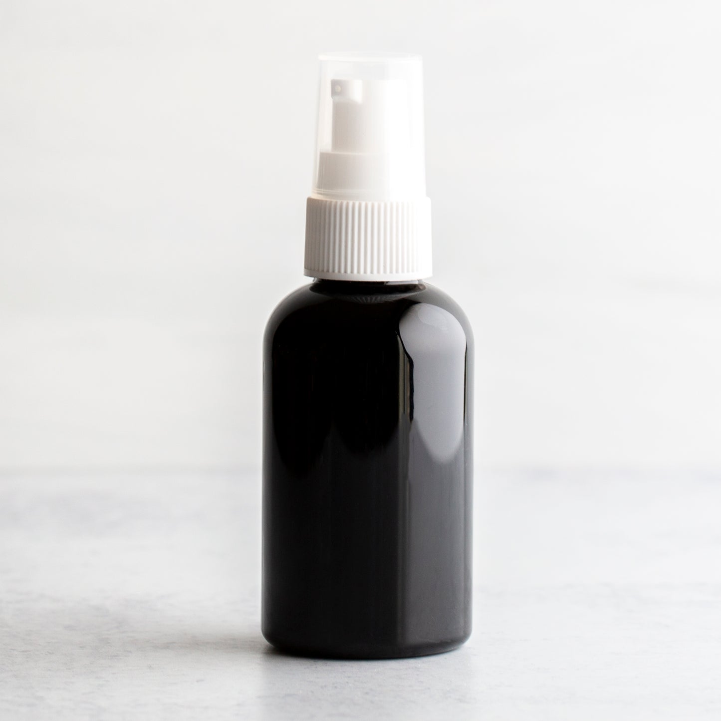 2 oz Black PET Boston Round Bottle with 20-410 White Treatment Pump